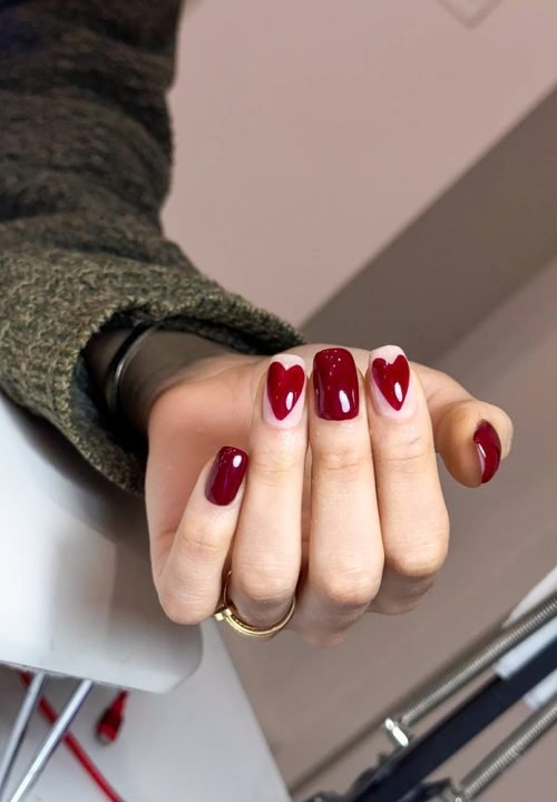 Portrait of a woman's hand with burgundy red nails featuring heart designs. Burgundy nails, Heart nail art, Elegant manicure, Valentine's nails
